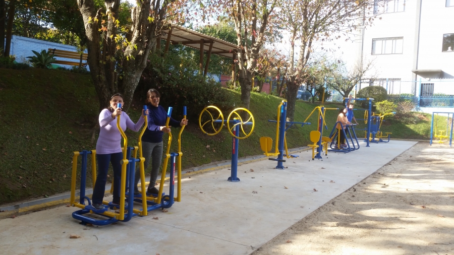 Na imagem, vários usuários encontram-se se exercitando nos aparelhos de ginástica instalados na entidade. À esquerda da imagem, duas mulheres utilizando o equipamento de simulação de caminhada com apoio para as mãos e, mais ao fundo outra dupla de usuários utilizando  aparelhos de ginástica instalados na entidade. À esquerda da imagem, duas mulheres utilizando o equipamento de simulação de caminhada sem o apoio para as mãos.